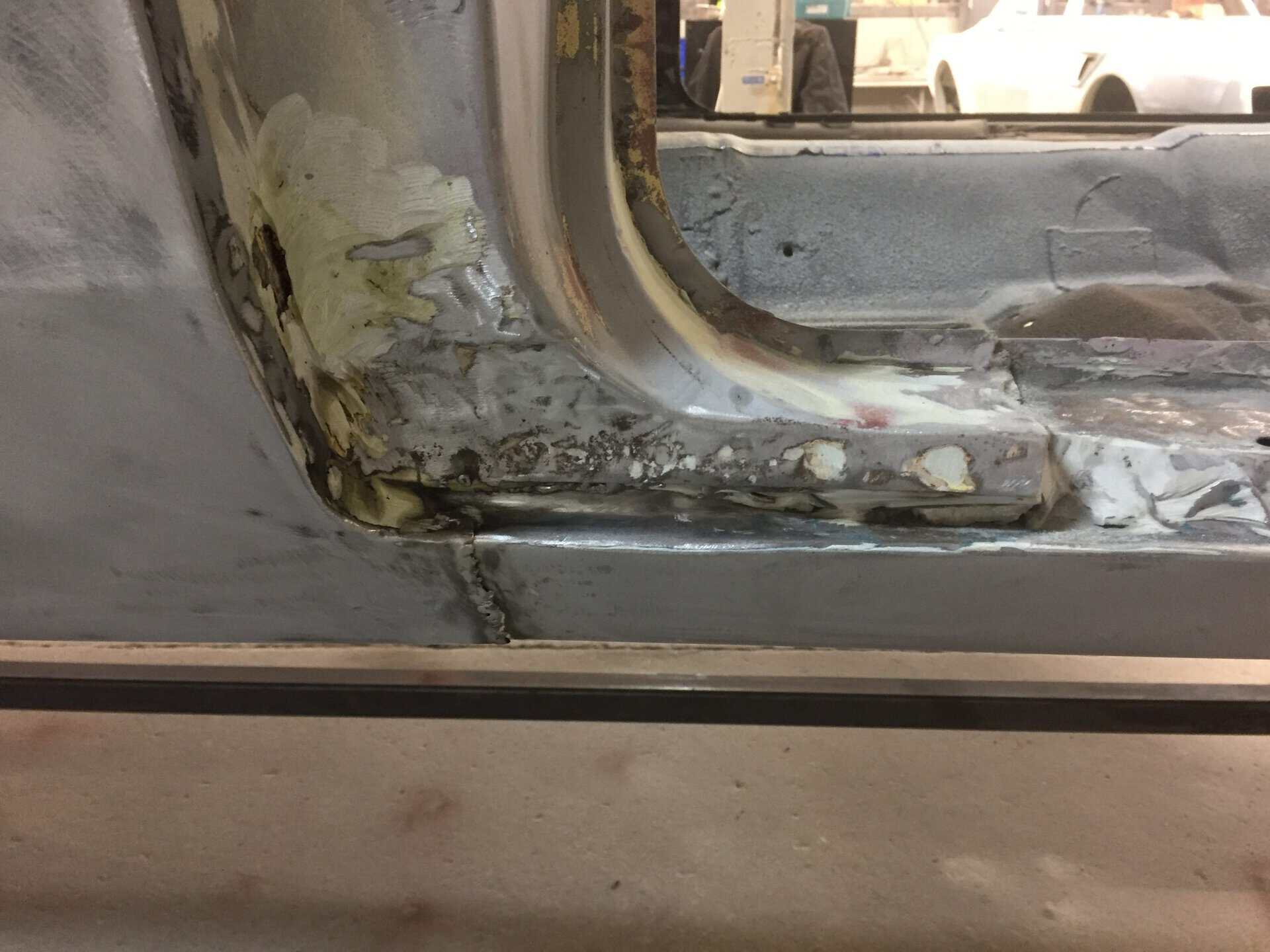 Close-up of car door frame with rust and bodywork in progress.