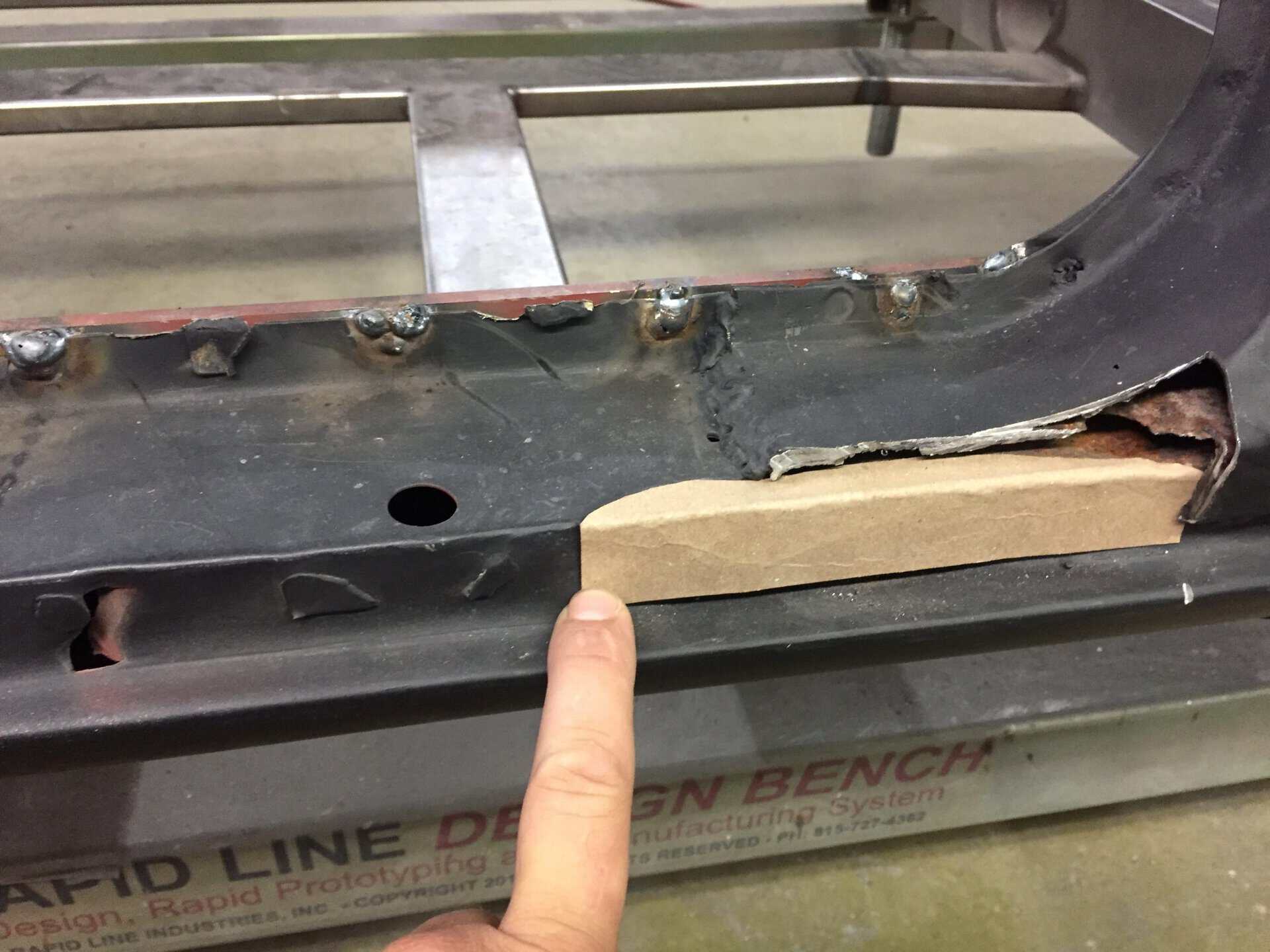 Close-up of car body panel repair with welding marks and rust damage.