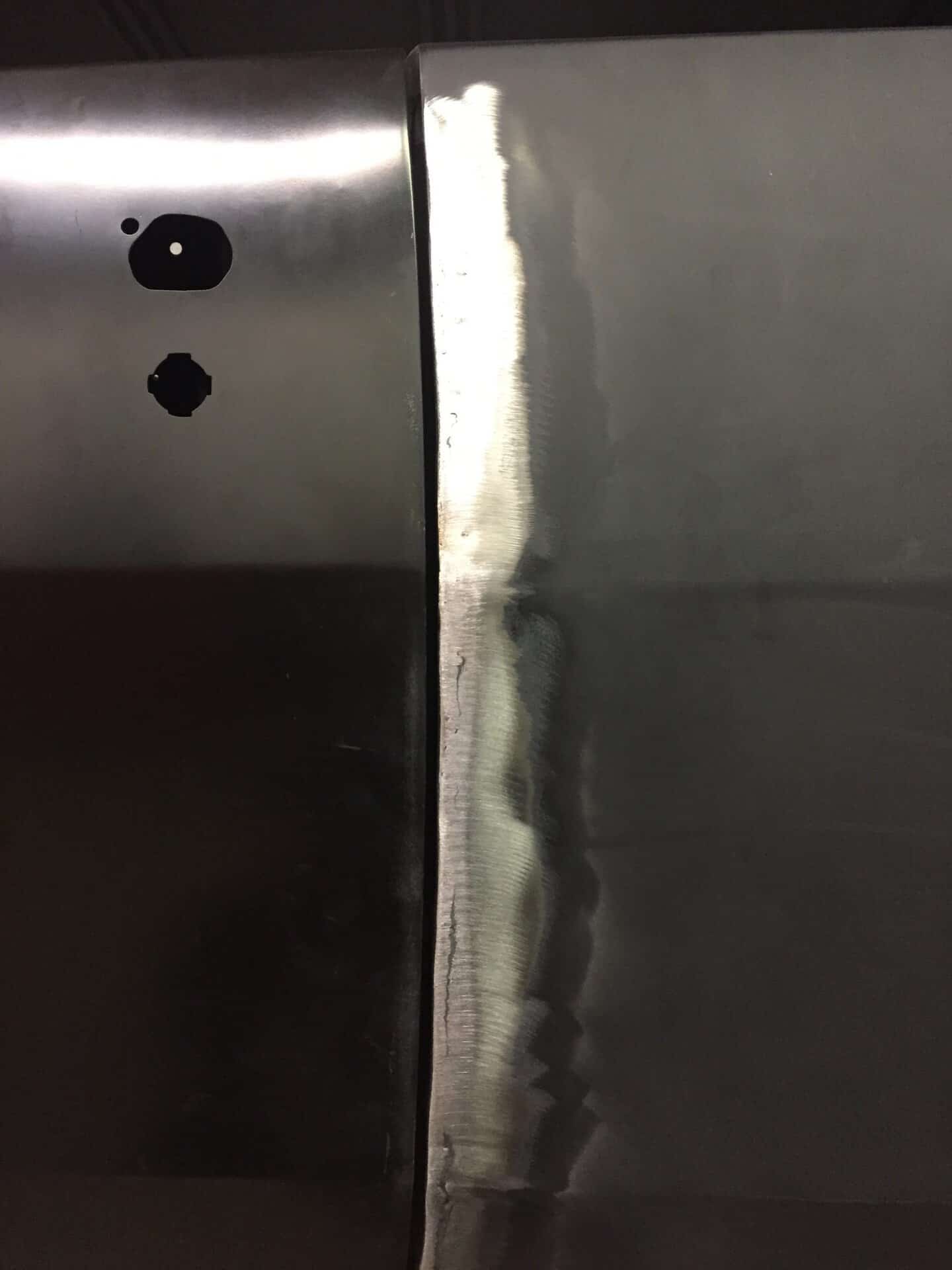 Close-up of metal panel with welding marks and holes.
