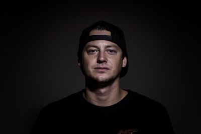 Young man wearing a black cap and black shirt against a dark background.