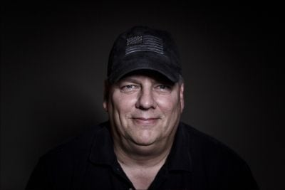 Man wearing black cap and black shirt, smiling at camera.