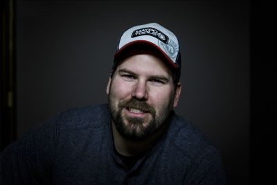 Man with a beard wearing a cap, smiling at the camera.