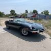 Vintage Jaguar E-Type convertible parked outdoors at All Speed Customs, a renowned car customization and repair shop.