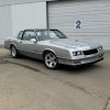 Classic Chevrolet Camaro IROC-Z in silver, customized with aftermarket wheels, parked outside a garage.