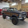 Jeep Grand Wagoneer with off-road tires and custom wood paneling at All Speed Customs workshop.