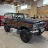 Jeep Grand Wagoneer with off-road tires and custom wood paneling at All Speed Customs workshop.