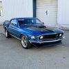 Vintage blue muscle car parked outside industrial building.