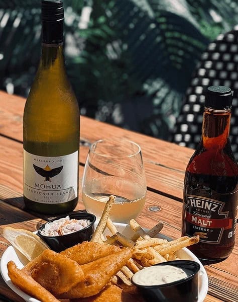 Wine, beer, and fried fish with dipping sauces on a wooden table.