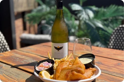 Delicious fried fish with lemon, coleslaw, and a bottle of wine on a rooftop table.