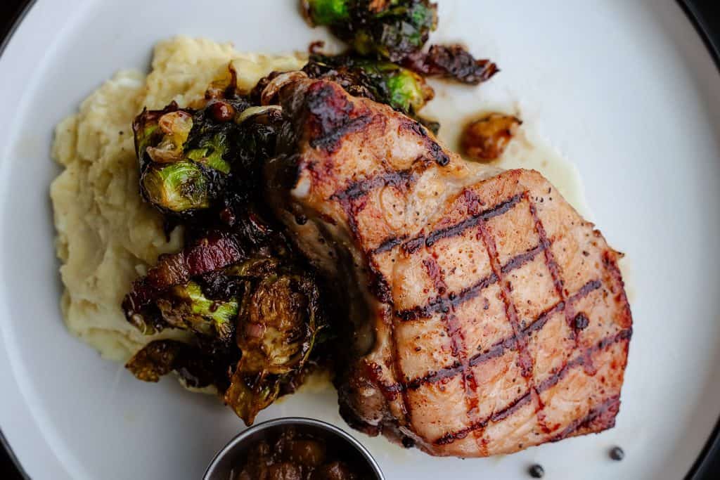 Juicy grilled pork chop served with mashed potatoes and sautéed vegetables on a white plate.