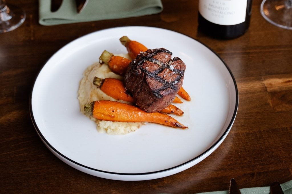 Juicy grilled steak served with roasted carrots and potatoes on a white plate.
