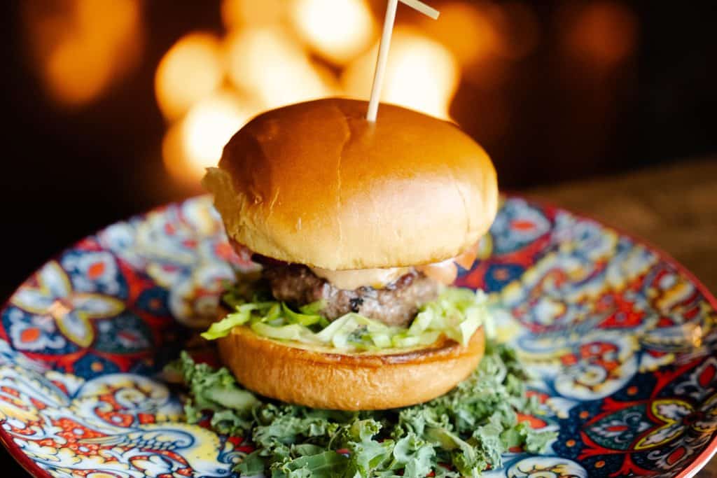 Juicy cheeseburger with lettuce on a colorful decorative plate at Attwood's Kitchen & Drink.