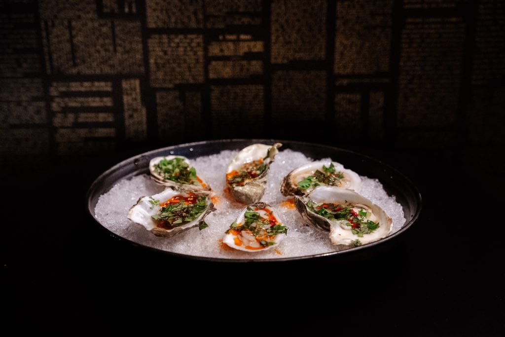 Fresh oysters on ice with herbs and sauce at Attwood's Kitchen & Drink, perfect for seafood lovers.