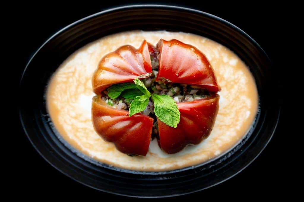 Fresh tomato caprese salad with basil on a black plate, creamy cheese, and herbs.