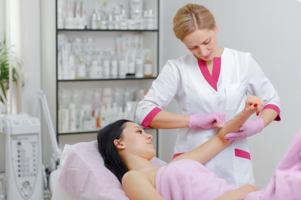 Beautician in pink gloves waxing a client's arm in a salon
