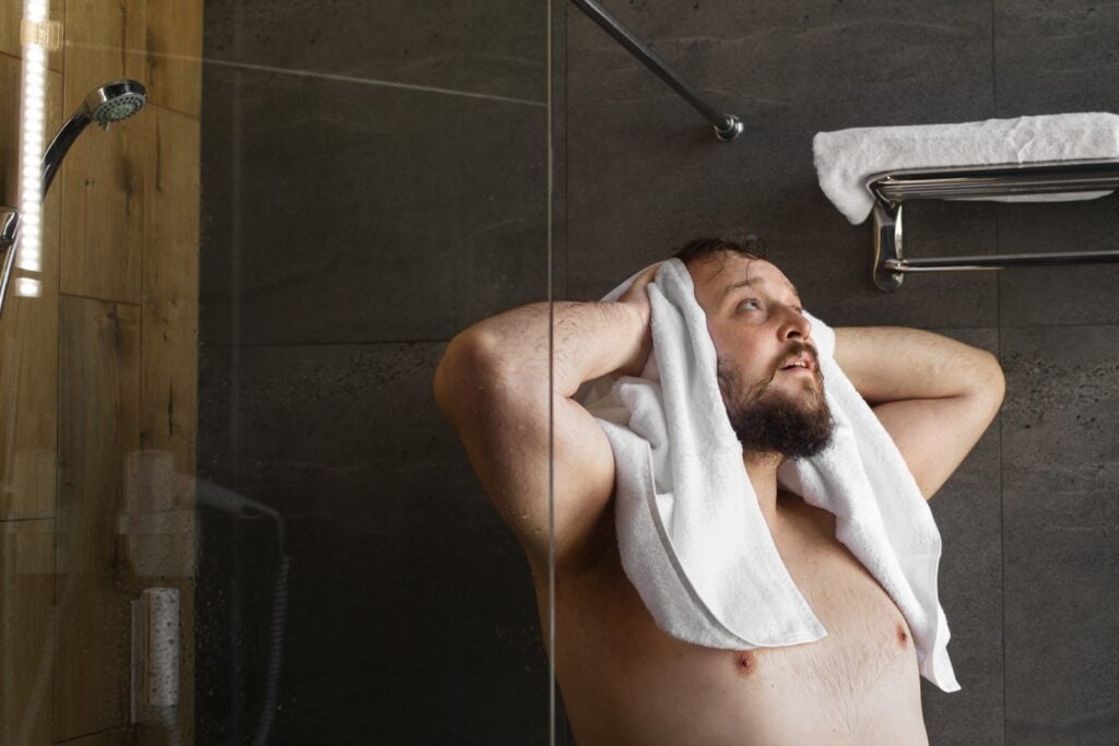 Bearded man drying his head with a white towel in a walk-in shower