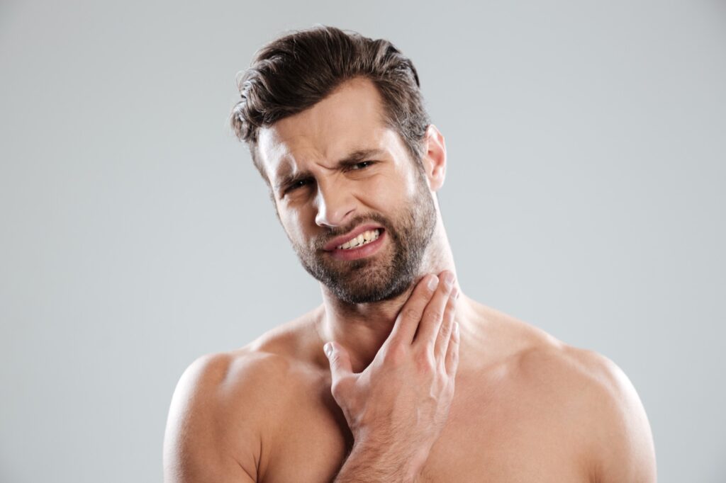 Shirtless man wincing with his hand pressed to the side of his neck