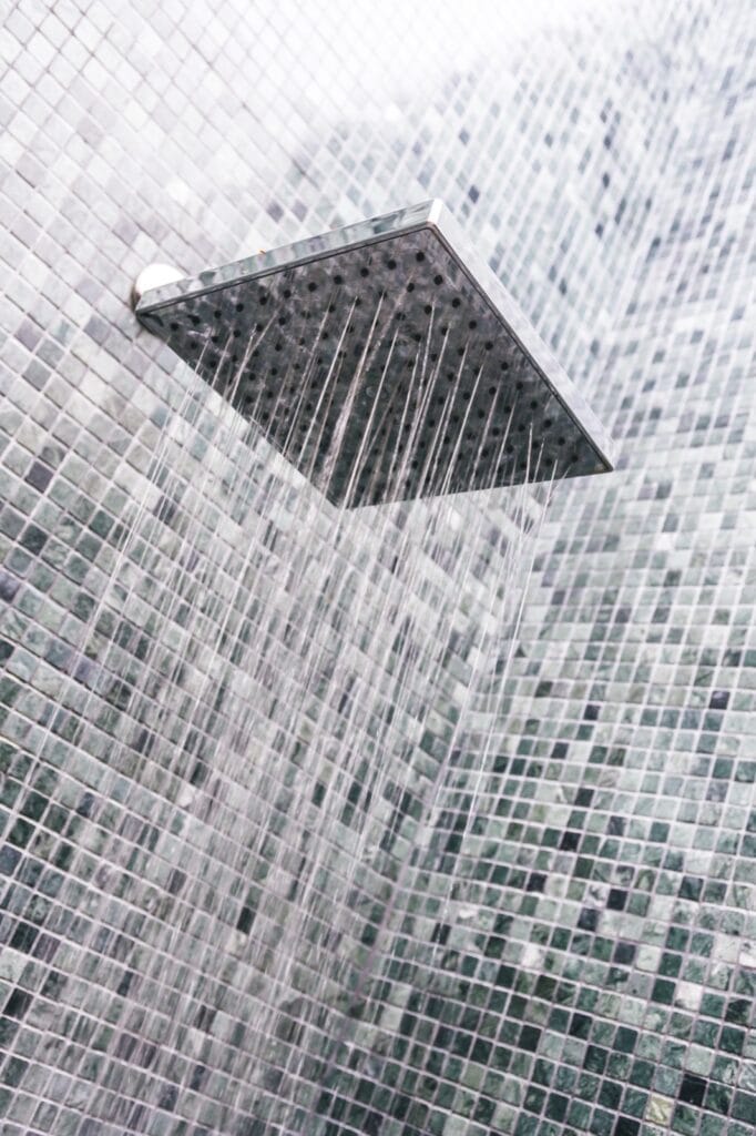Square shower head with water running against green mosaic tiles