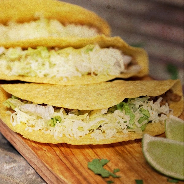 Delicious fish taco with shredded cabbage and lime wedges on a wooden board.