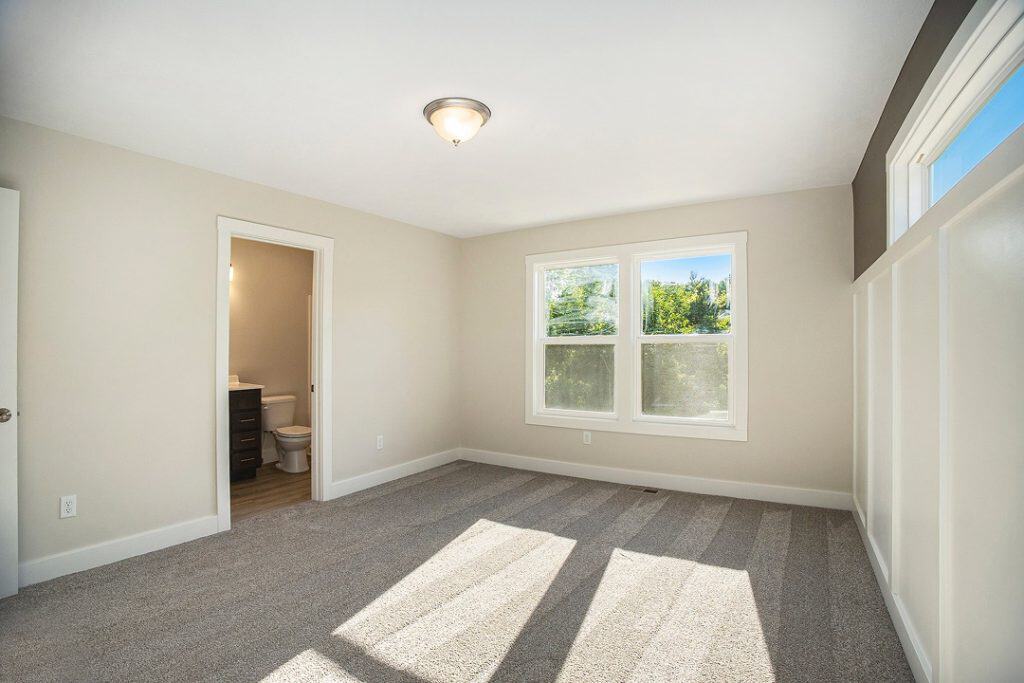 Spacious bedroom with large windows and attached bathroom in a new home.