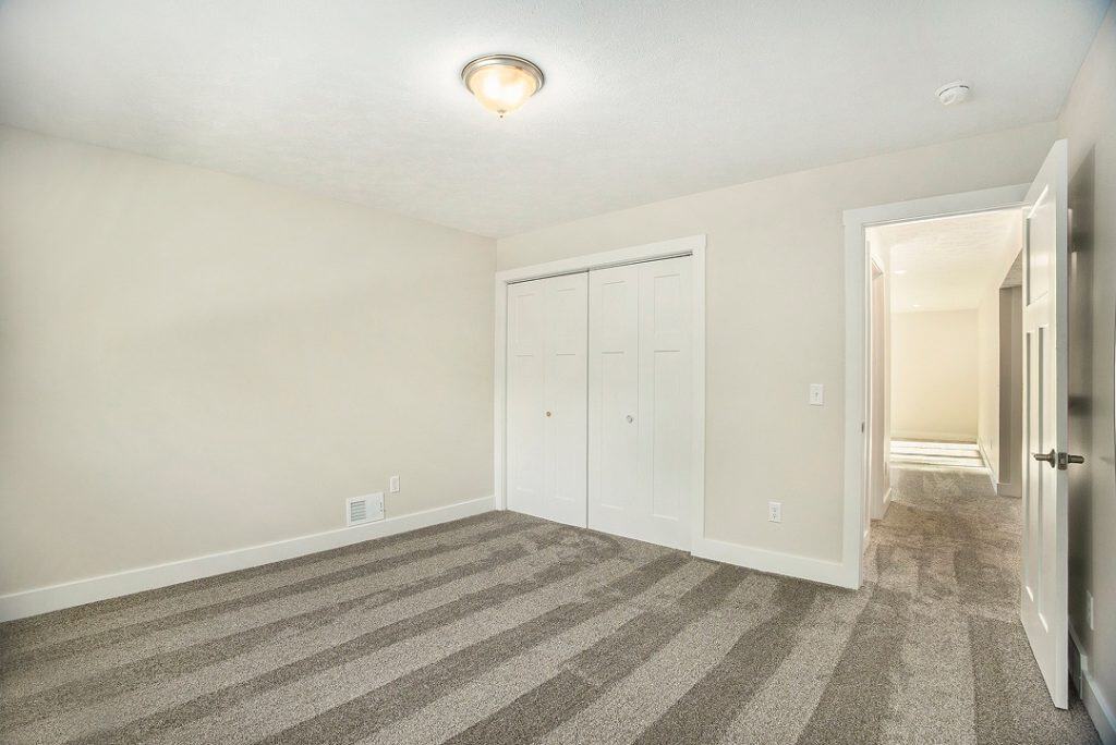 Spacious bedroom with neutral walls and plush carpet flooring.