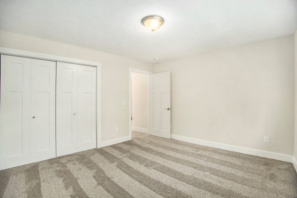 Empty bedroom with white walls and beige carpet in a new home.