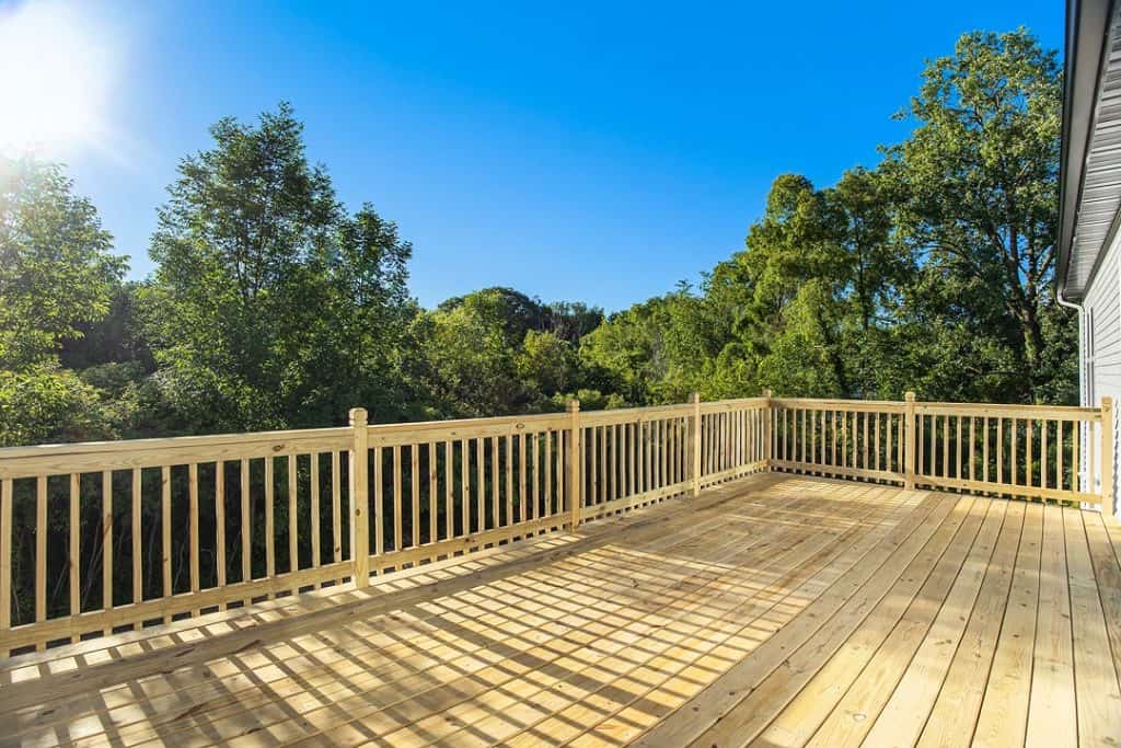 Spacious wooden deck with railing overlooking lush green trees.