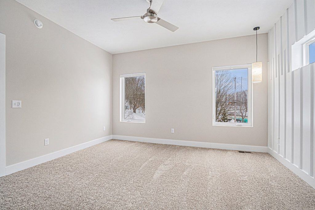 Bright empty room with large windows and ceiling fan in a custom home.