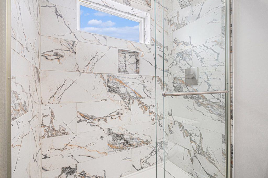 Modern marble shower with window and glass door in a new home.
