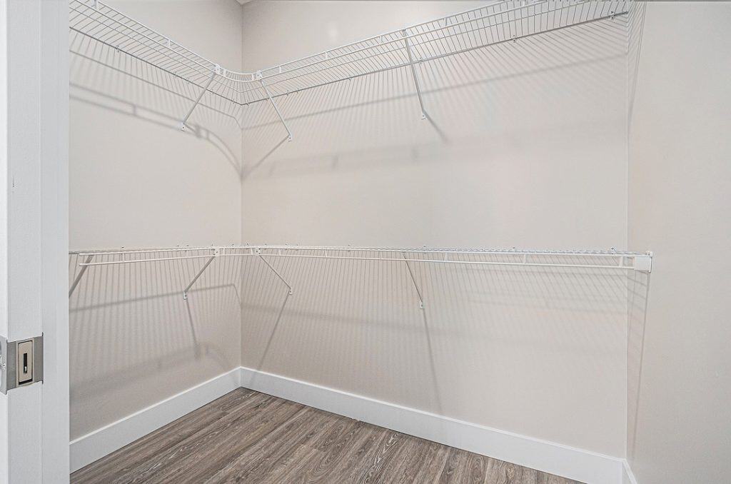 Empty walk-in closet with white wire shelving and wood flooring.