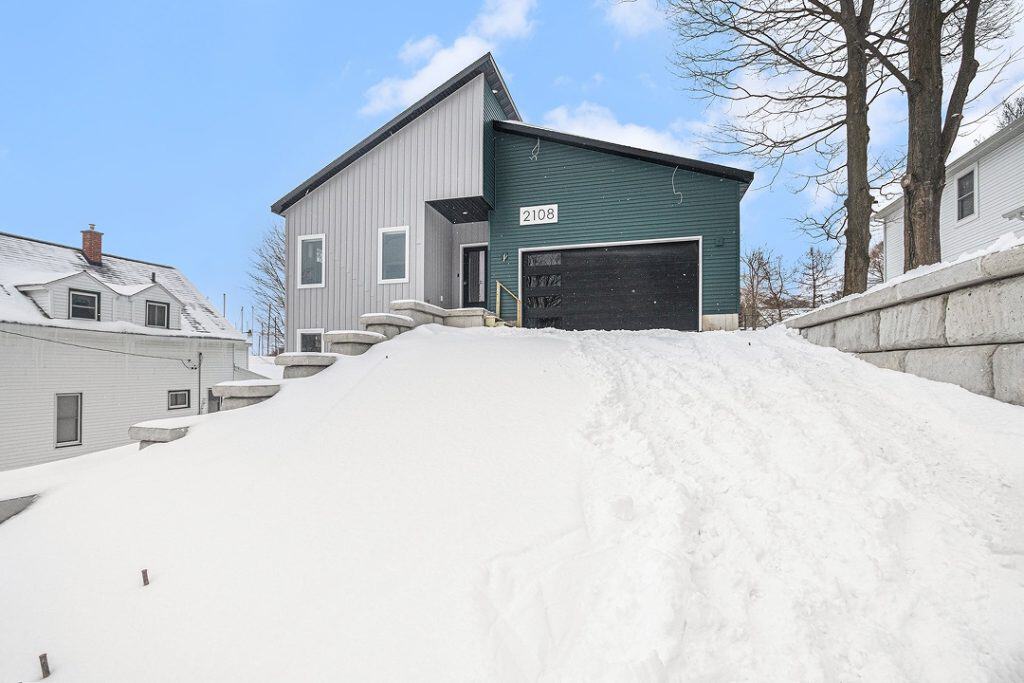 Contemporary house with green and gray exterior in snowy setting.