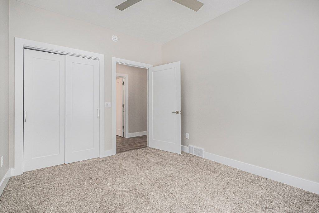 Empty bedroom with white walls, closet, and beige carpet flooring.