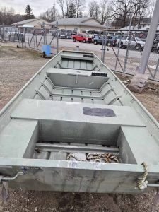 Aluminum fishing boat parked outdoors near a chain-link fence.