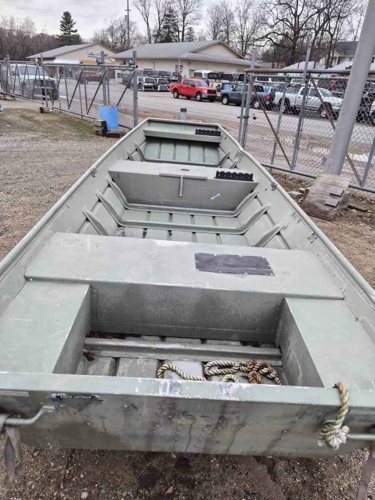 Aluminum fishing boat parked outdoors near a chain-link fence.