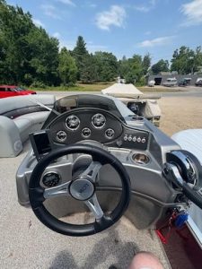 Boat dashboard with steering wheel and gauges on a sunny day.