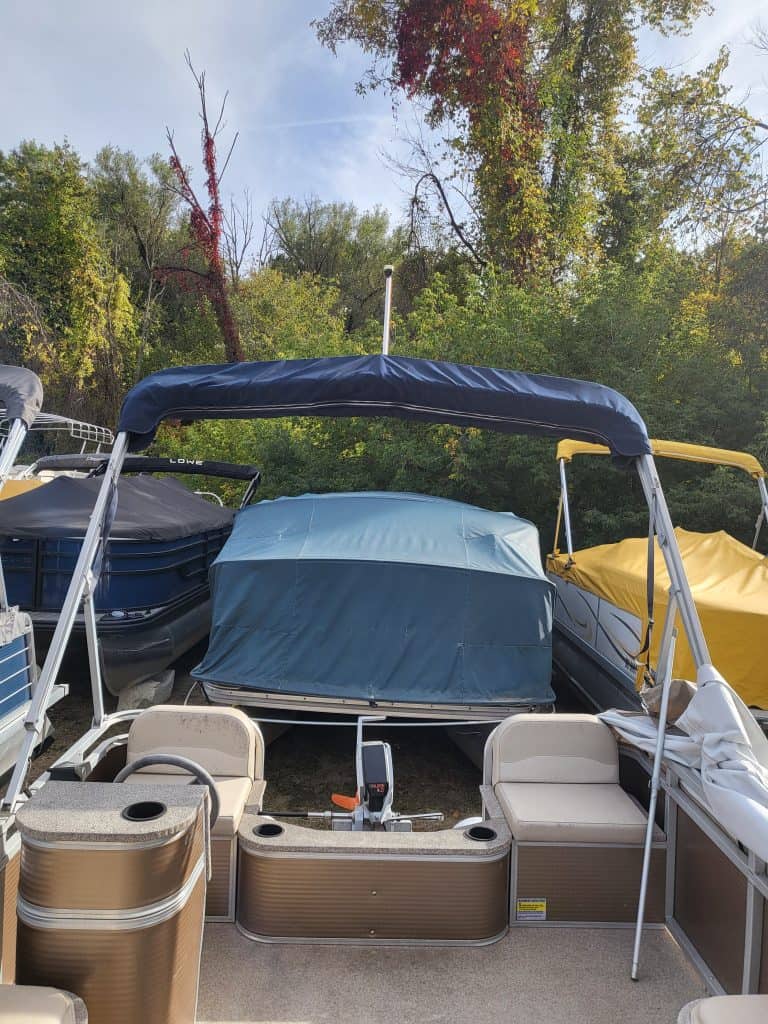Pontoon boat displayed outdoors amidst fall foliage, highlighting boating gear and accessories.