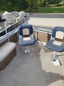 Aluminum boat seats with cushioned chairs and side panels on a sandy surface.