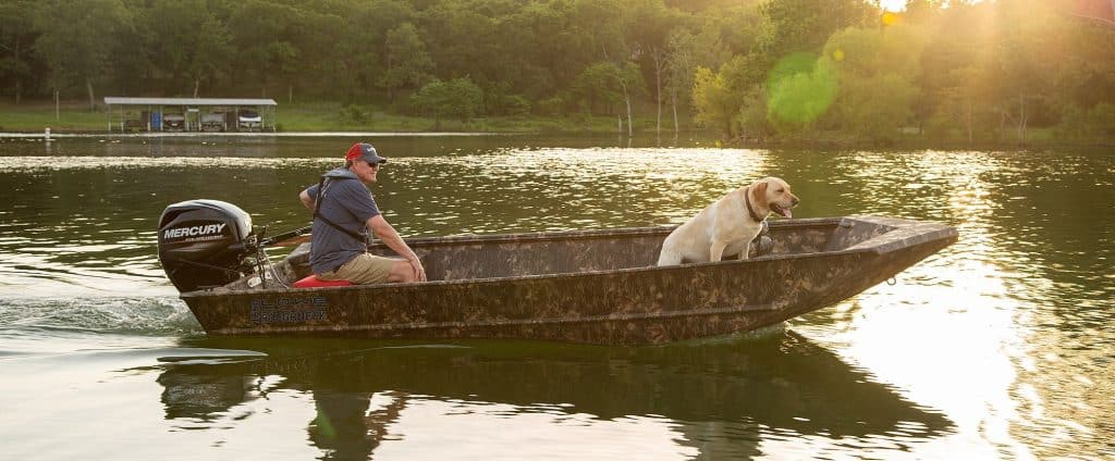 Man and dog enjoying a boat ride on a calm lake at sunset.