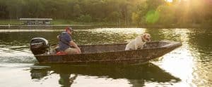 Man and dog enjoying a boat ride on a calm lake at sunset.