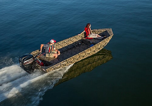 Two people in a small aluminum boat on calm water with outboard motor.