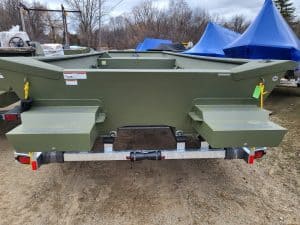 Green aluminum boat on trailer with blue covers in background.