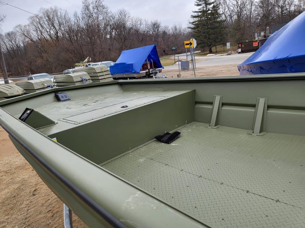 Empty boat interior with green flooring and storage compartments.