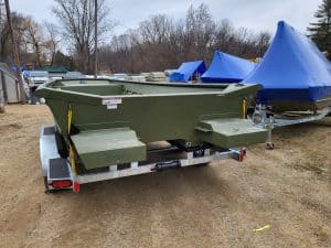 Green boat on trailer at Camp and Cruise with covered boats in background.