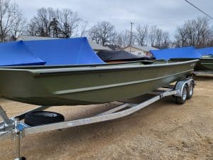 Green boat on trailer at Camp and Cruise with blue covers.