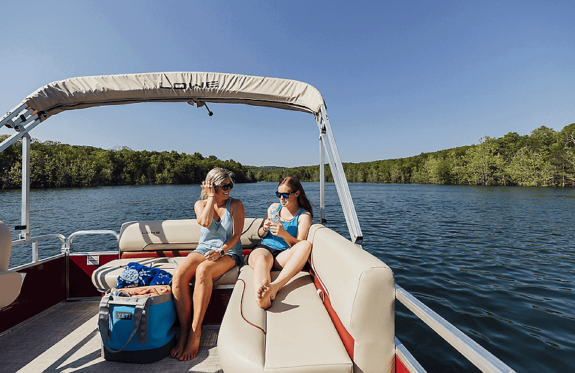 Two women relaxing on Lowe Boats UF162 pontoon boat on a lake.
