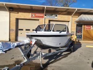 White boat on EZ Loader trailer outside marine shop with Mariner Outboards sign.