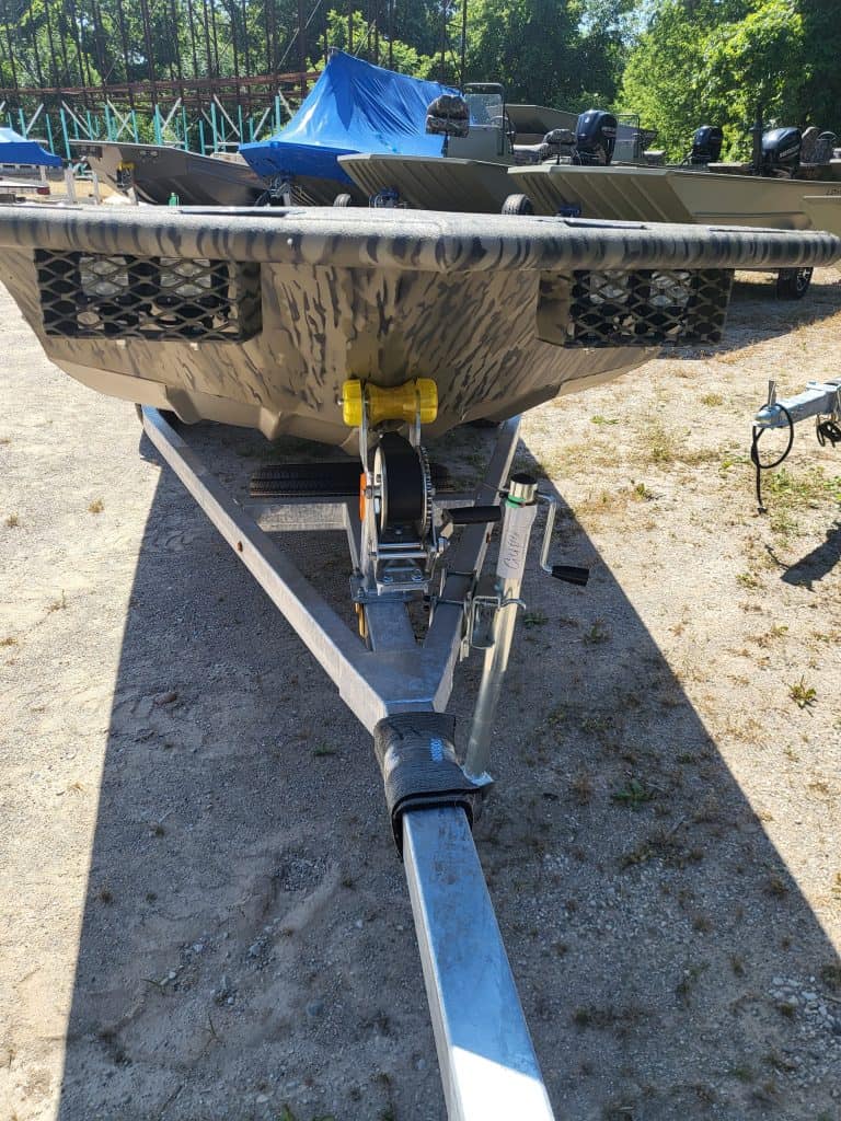 Camouflage boat on trailer with outboard motors and blue cover.