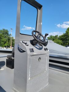 Boat console with steering wheel and controls on a clear day.