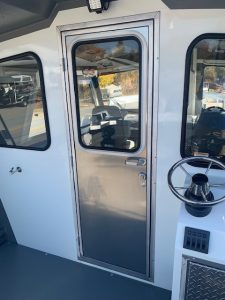 Boat door with window and steering wheel inside the vessel.