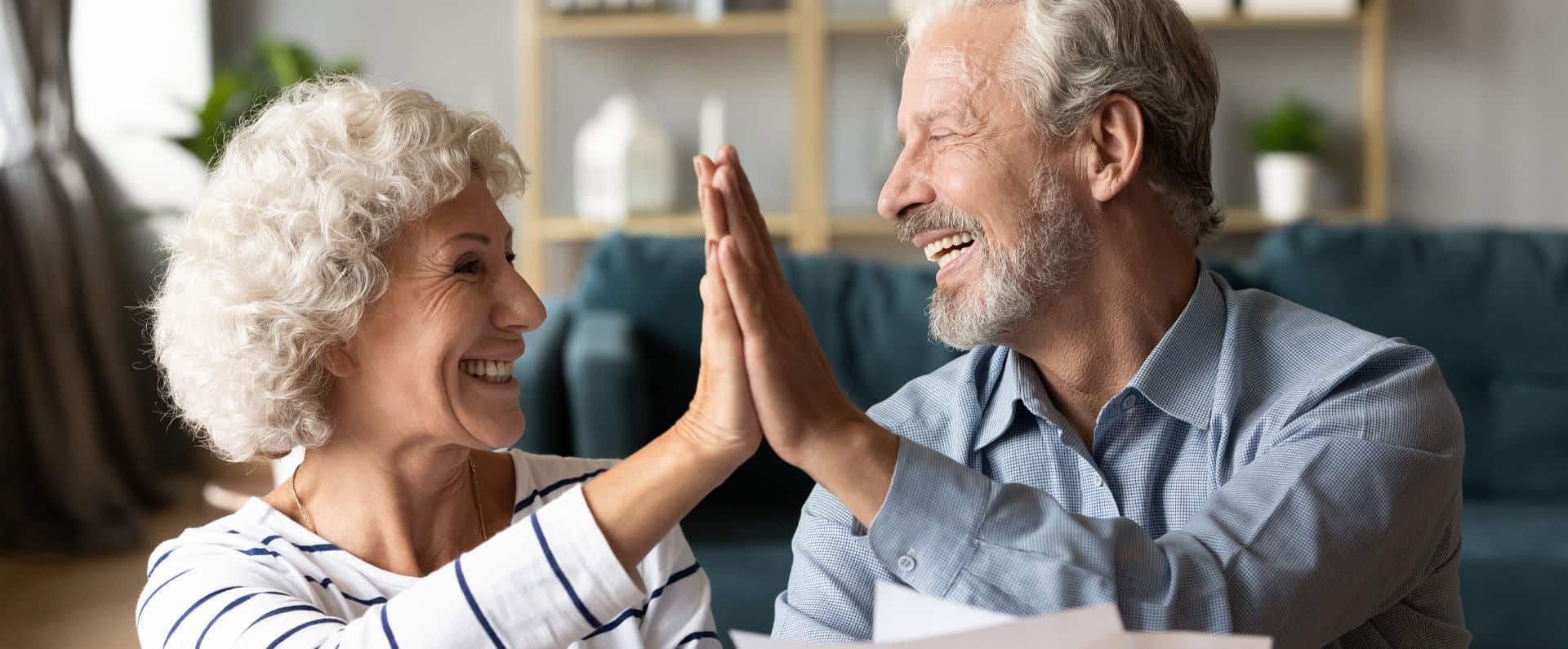 Senior couple celebrating with high-five in living room.